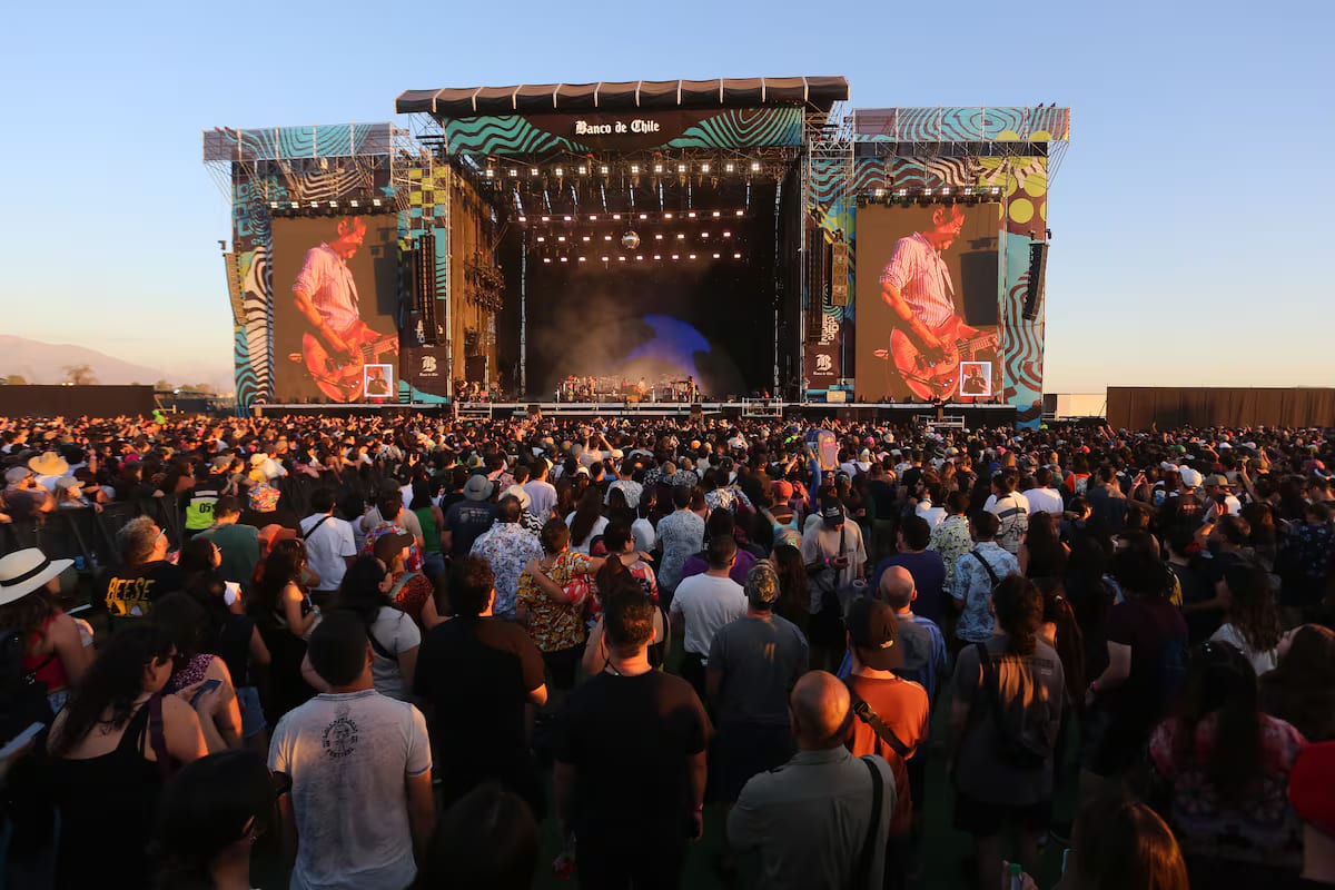 A dense festival crowd with hands raised in front of a main stage at golden hour