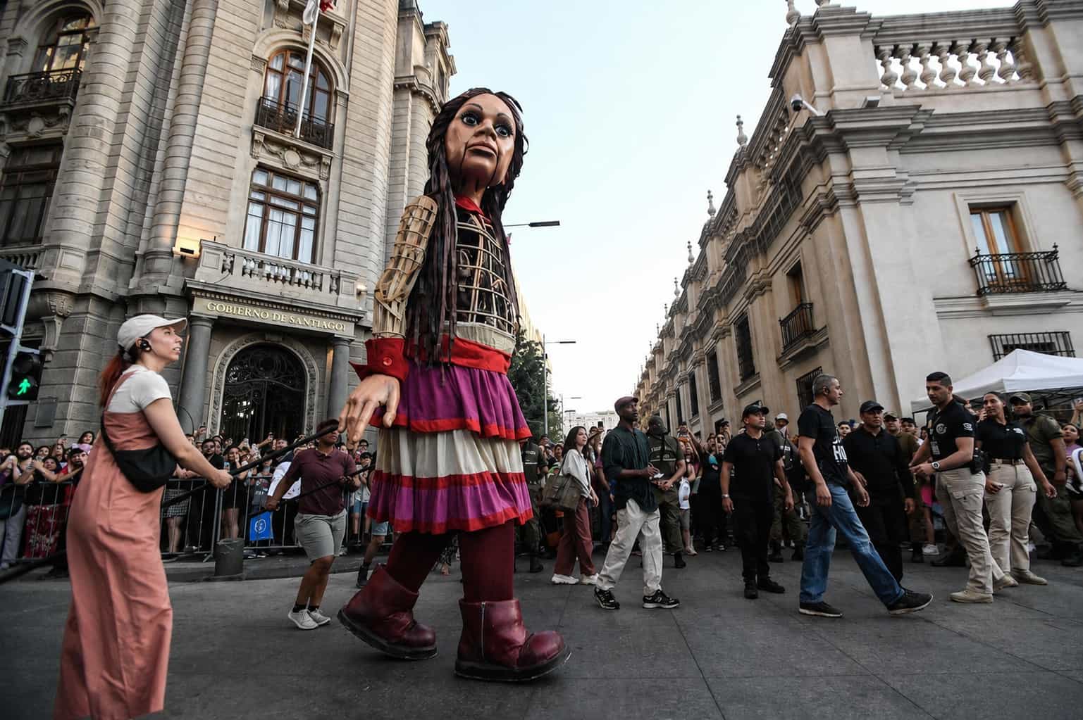 An enormous puppet moving down a closed street in central Santiago, crowds pressed to both pavements at dusk