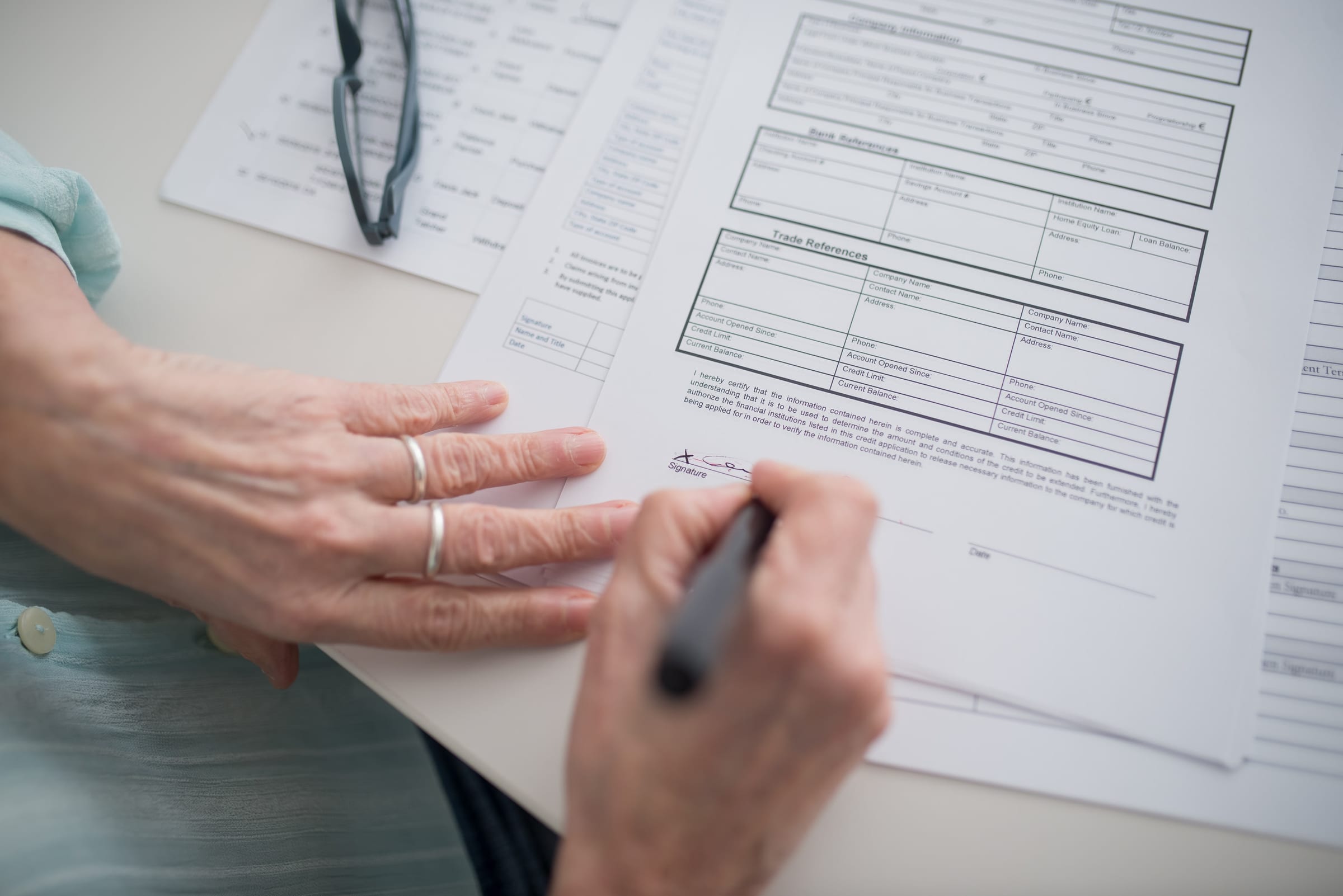 A close-up view of a hand signing official documents with a pen indoors