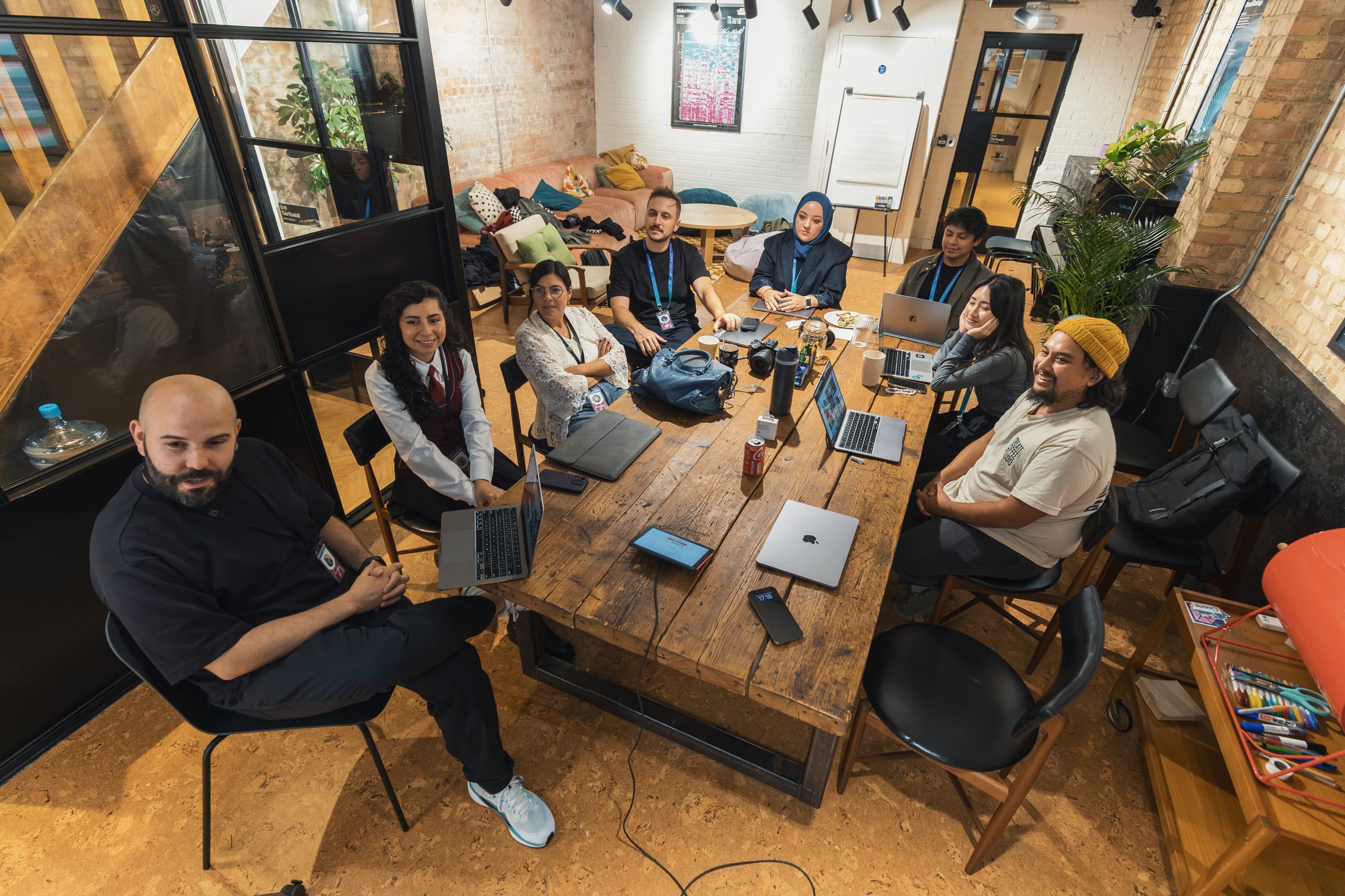 Group of colleagues gathered around a table in a modern coworking space, collaborating on laptops